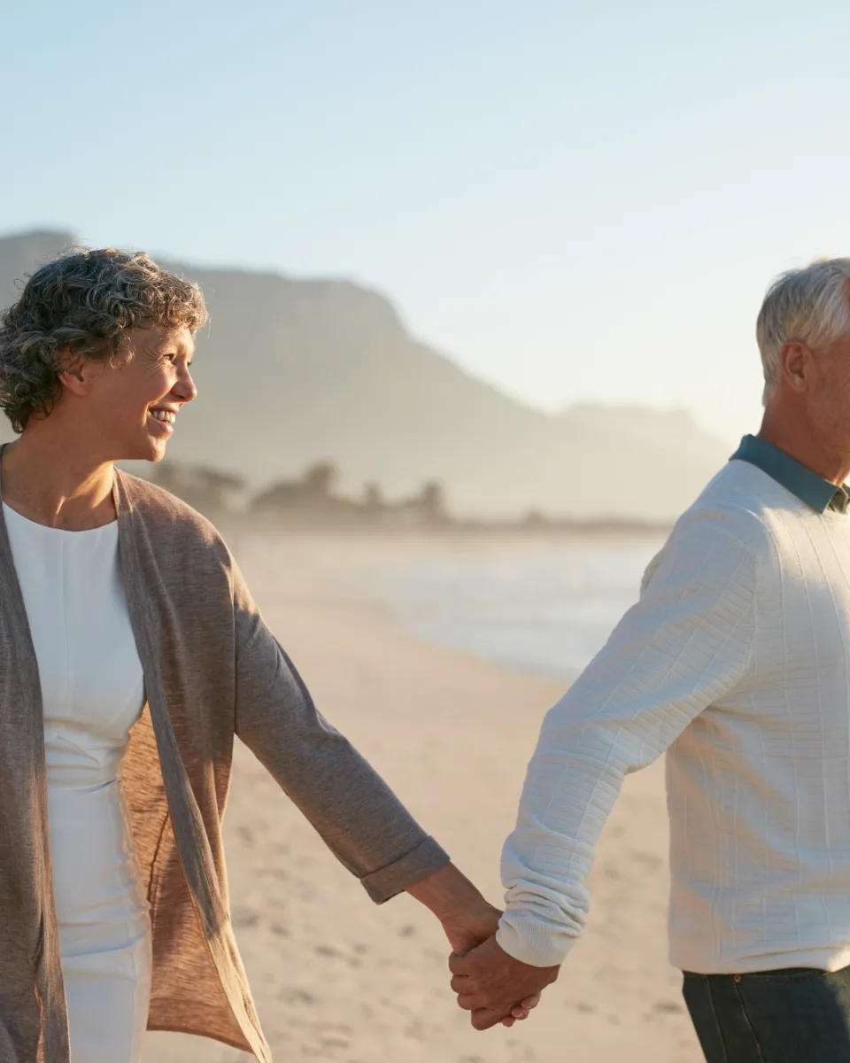 An older couple walking along a beach at sunset