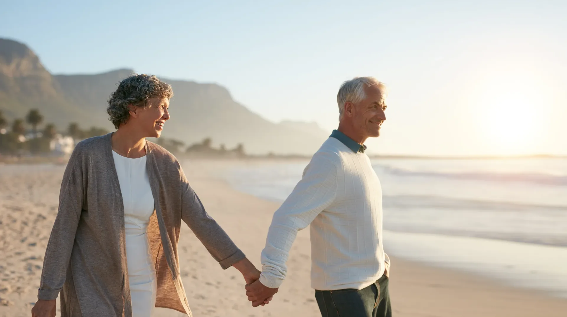 An older couple walking along a beach at sunset